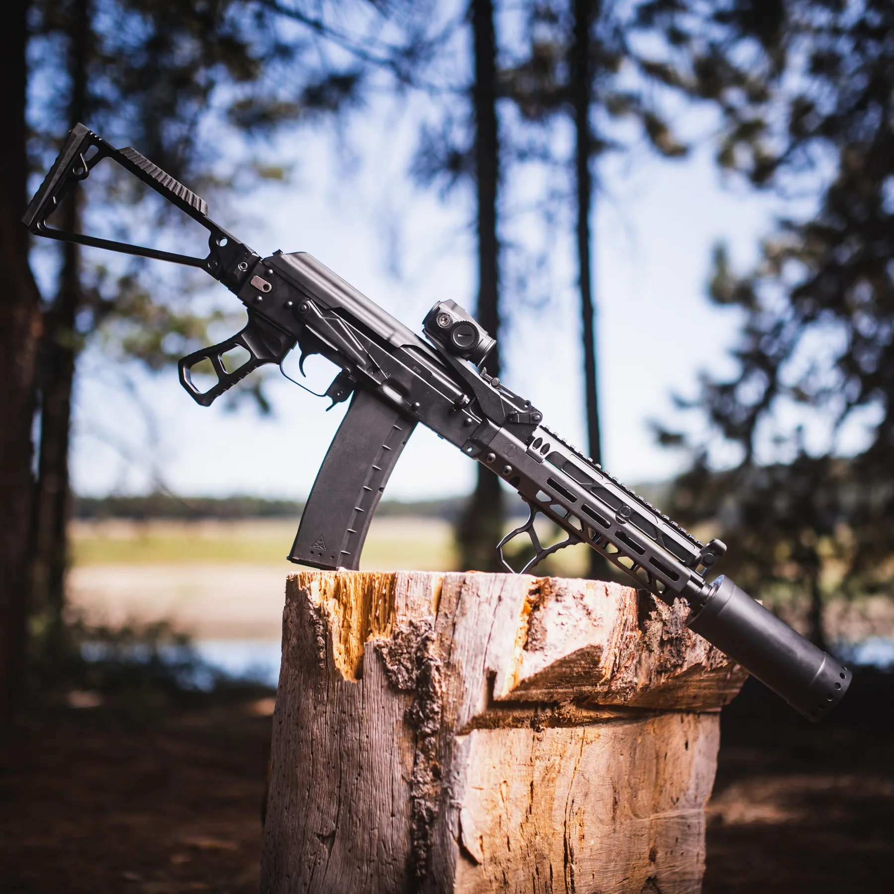 Suppressed rifle resting on a stump in the pines