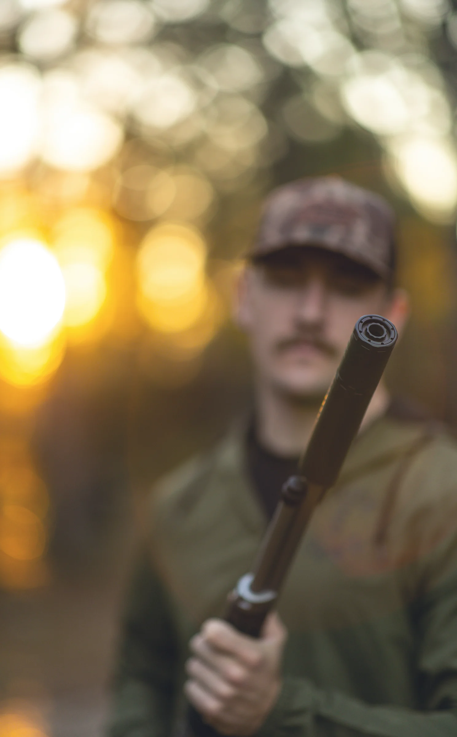 Suppressor endcap sharp in the foreground, shooter soft behind at golden hour