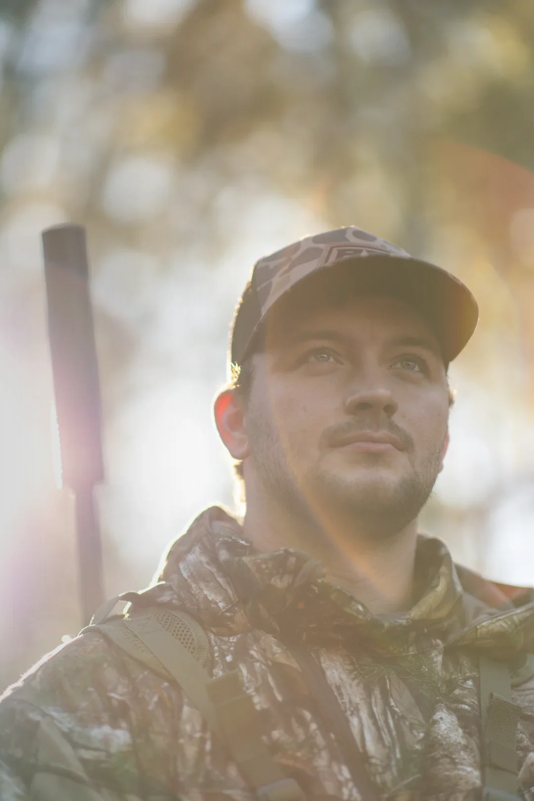 Hunter in camo at golden hour with a suppressed rifle on his shoulder