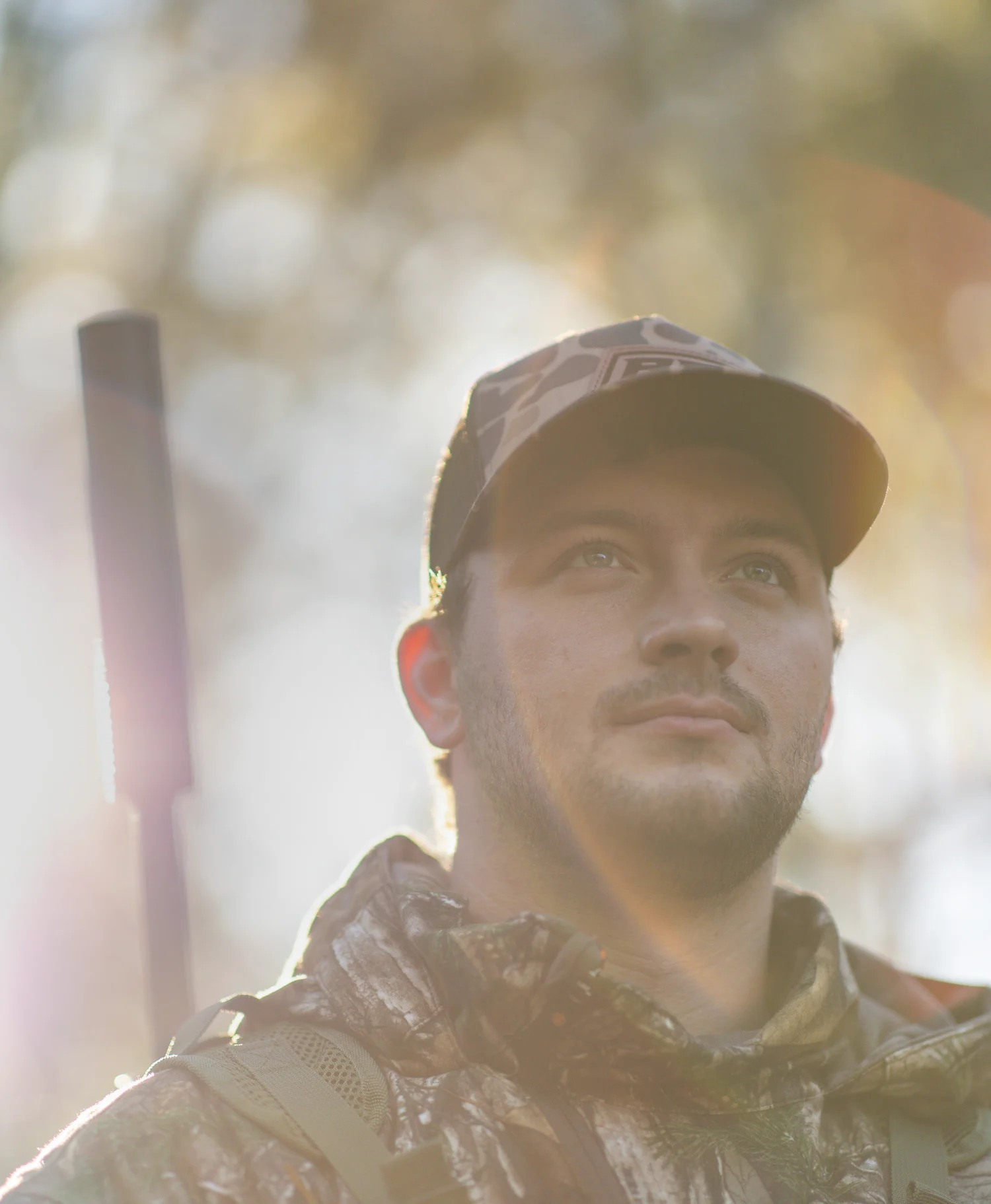 Hunter in camo at golden hour with a suppressed rifle on his shoulder